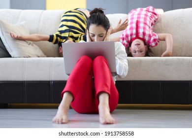 Tired Woman With Laptop Sits On Floor With Closed Palms Ears Behind On Couch Children Indulge. Remote Work In Coronavirus Pandemic Concept