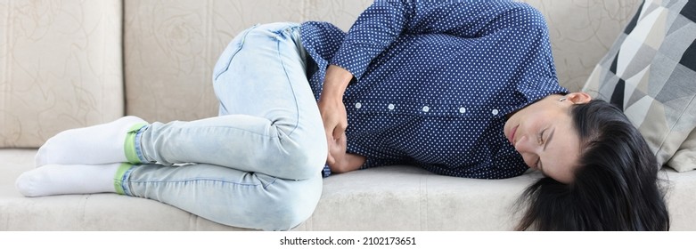 Tired Woman Lies On Couch With Abdominal Pain. Pain In Lower Abdomen In Women Concept