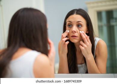 Tired Woman Looking At Her Eye Bags In The Bathroom.