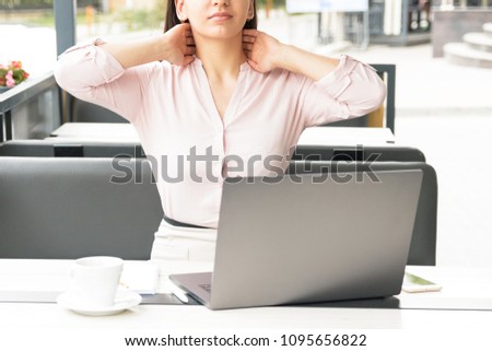 A tired woman massaging her neck at desktop in office.