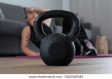 Tired woman resting on a floor after heavy intense exercise. Focus on gym kettlebell equipment. House fitness workout, sport training concept. Exhausted sporty female taking a break at home.