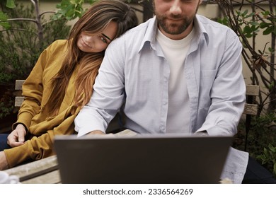 Tired Woman Resting on Partner's Shoulder in Cafe - She watches as he continues typing on a laptop. - Shutterstock ID 2336564269
