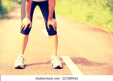 Tired Woman Runner Taking A Rest After Running Hard In Countryside Road. Sweaty Athlete After Marathon Training In Country Road. 