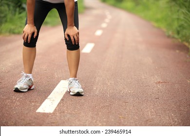 Tired Woman Runner Taking A Rest After Running Hard In Countryside Road. Sweaty Athlete After Marathon Training In Country Road. 