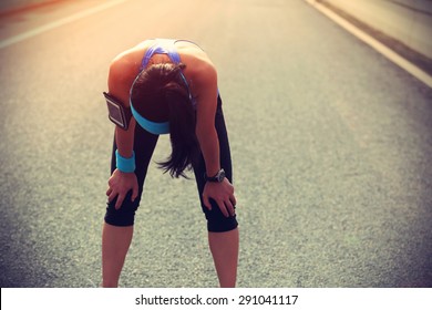 Tired woman runner taking a rest after running hard on city road