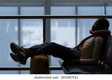 Tired Woman Sleep In Airport On Chair With Legs On Suitcase Waiting For Transit Flight Departure. Black Traveler Female Passenger Nap In Modern Terminal After Plane Cancellation Or Bad Weather Delay