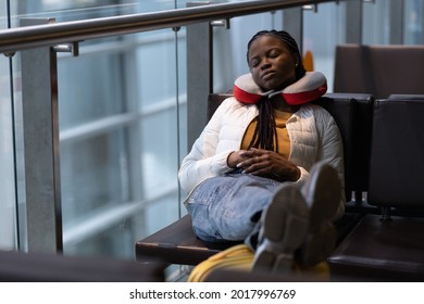 Tired Woman Sleep In Airport On Chair With Legs On Suitcase Waiting For Transit Flight Departure. Black Traveler Female Passenger Nap In Modern Terminal After Plane Cancellation Or Bad Weather Delay