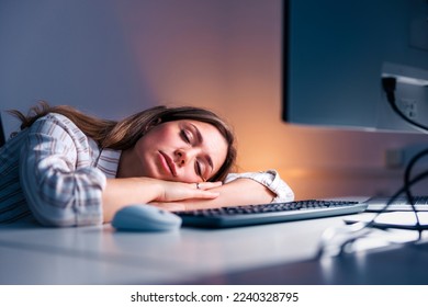 Tired woman sleeping at her desk while working late in an office; woman leaning on her desk and taking a power nap while working overtime