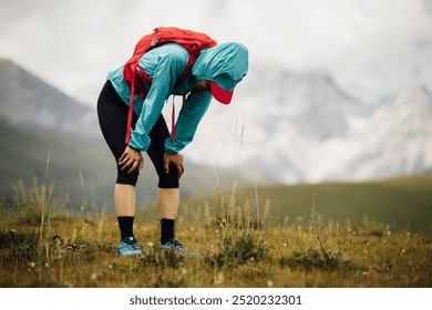 Tired woman trail runner running in grassland with snow capped mountains in the background - Powered by Shutterstock