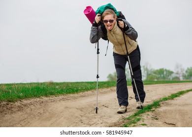 tired woman with trekking pole in hand , walking with a heavy backpack outdoors