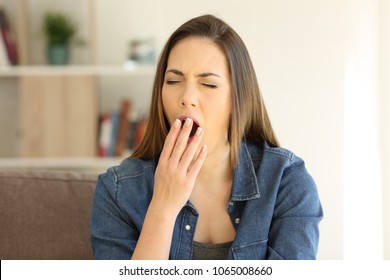 Tired woman yawning covering mouth sitting on a couch in the living room at home