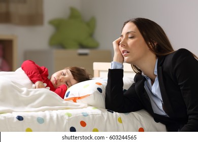 Tired worker mother wearing suit sleeping beside her sleepy daughter on a bed at home