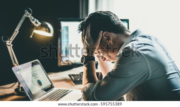 Tired and worried\
business man at workplace in office holding his head on hands after\
late night work, concept