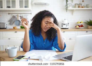 Tired young African American single mother feeling stressed because of financial problems, working through finances in kitchen late at night, doesn't have enough money to pay off mortage debt