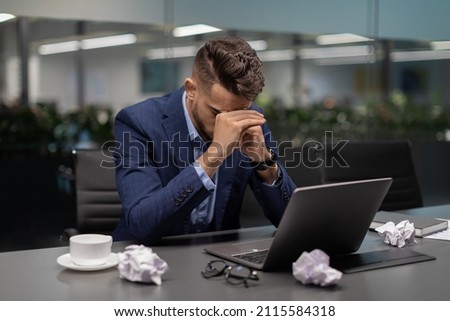 Tired young arab man financial manager sitting at worktable in front of computer, looking for creative solutions while crisis, modern office interior, copy space, difficulties with business concept