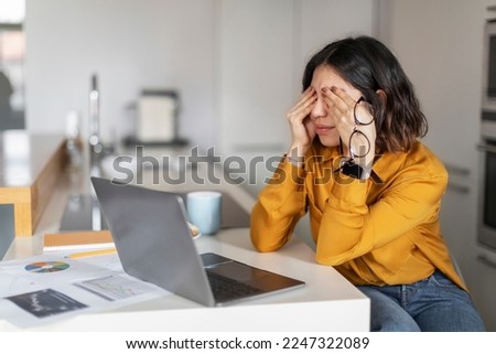 Tired Young Arab Woman Feeling Eyes Strain After Using Laptop At Home, Millennial Middle Eastern Female Freelancer Sitting At Desk With Computer In Kitchen And Rubbing Eyelids, Closeup Portrait