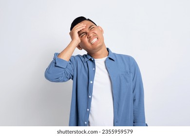 Tired young Asian man in casual shirt suffering from headache or migraine, massaging his temples with closed eyes isolated on white background - Powered by Shutterstock