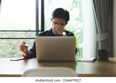 Tired Young Asian Man Feel Pain Eyestrain Holding Glasses Rubbing Dry Irritated Eyes Fatigued From Computer After Work, Stressed. Man Suffer From Headache Bad Vision Sight Problem Sit At Home.