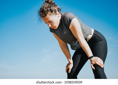 Tired young athletic woman runner taking a rest, doing break, breathing hard after running hard outdoors, standing on blue sky background. Weight loss cardio goal achievement challenge. Copy space - Powered by Shutterstock