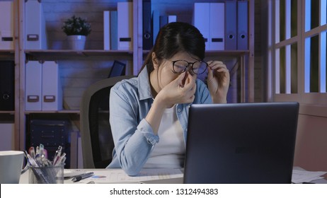 Tired Young Freelance Worker Rubbing Her Eyes While Sitting In Front Of Laptop Computer And Working On Promising Project. Girl Soho Lady Stay Up Late In Home Office Holding Glasses Eye Painful.