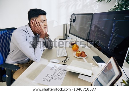 Tired young Indian programmer almost sleeping at his desk after working on difficult project all day long