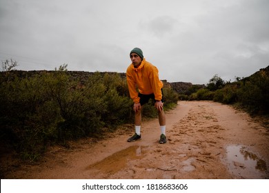 Tired Young Male Trail Runner Resting After Sprinting Down Wet Mountain Trail In Cloudy Weather With Rain And Foliage