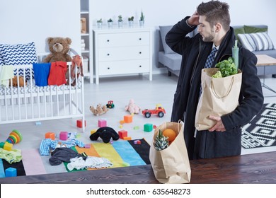 Tired Young Man Bringing Groceries Home And Looking At Messy Nursery