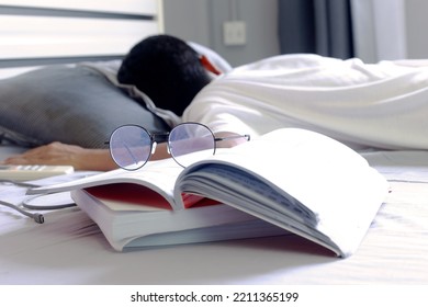 Tired Young Man  Deep Sleeping In A Bed - Exhaustion  From Work , Study Hard -  Selective Focus On Glasses On Heap Of Books.