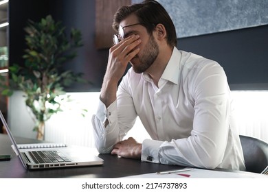 Tired young man feel pain eyestrain holding glasses rubbing dry irritated eyes fatigued from computer work, stressed man suffer from headache bad vision sight problem sit at office