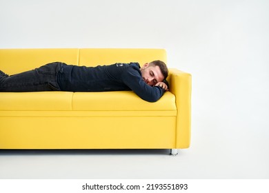 Tired Young Man Lying Down On Yellow Sofa Over White Background. Exhausted Concept