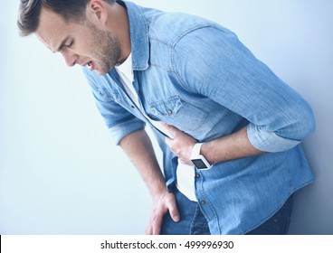 tired young man suffering from stomachache near the wall.