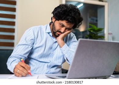 Tired Young Man While Working On Laptop By Taking Notes At Office Desk - Concept Of Job Frustration, Routine Work Life And Exhaustion.