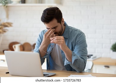 Tired young man work on laptop take off glasses massage eyes suffer from blurred vision or dizziness, exhausted millennial male feel unwell having headache migraine, overwork, health problem concept - Shutterstock ID 1733726783