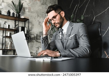 Tired young manager multitasking while working on laptop in modern office. Businessman exhausted CEO accountant lawyer dealing with financial issues, error and mistake at workplace concept