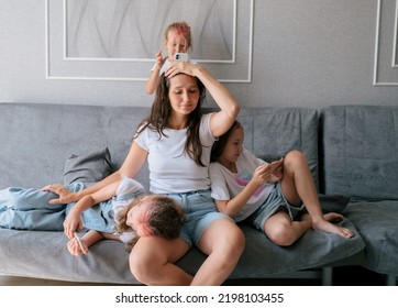 Tired young mother sits on couch and holds her head while her three naughty daughters play games on smartphones. lifestyle family together portrait.