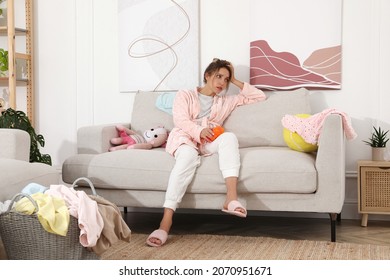 Tired Young Mother Sitting On Sofa In Messy Living Room