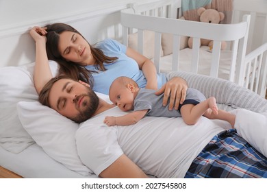 Tired Young Parents With Their Baby Sleeping In Bed At Home