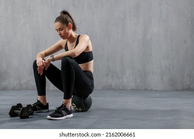 Tired Young Sporty Woman Having Rest After Workout, Sitting On Floor At Gym , Over Grey Background.