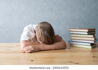 A tired young student rests his head on arms beside a stack of colorful books, symbolizing academic fatigue - Powered by Shutterstock