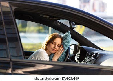 Tired Young Woman Asleep On Pillow On Steering Wheel, Resting After Long Hours Driving A Car. Fatigue. Sleep Deprivation. 