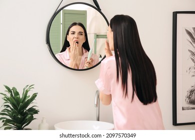 Tired Young Woman Brushing Teeth In Bathroom