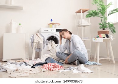 Tired young woman with dirty laundry near washing machine at home - Powered by Shutterstock