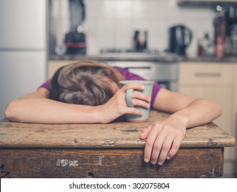 A tired young woman is having a cup of tea and is resting her head on a table