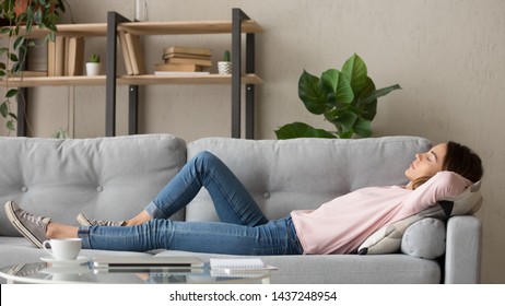 Tired young woman lying on cozy couch take nap daydreaming in living room, peaceful girl relax on comfortable sofa with eyes closed sleeping resting at home, female feel fatigue fall asleep
