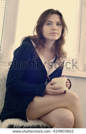 tired young woman on the balcony with a mug of tea. the white balance is incorrect.