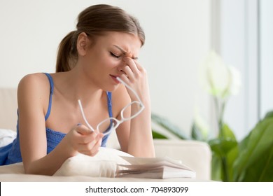 Tired young woman removing eyeglasses, massaging eyes after reading paper book, needs eye drops. Female student feeling discomfort because of long wearing glasses, suffering from eyes pain or headache