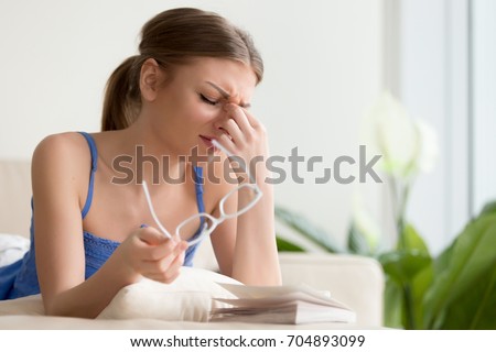 Tired young woman removing eyeglasses, massaging eyes after reading paper book, needs eye drops. Female student feeling discomfort because of long wearing glasses, suffering from eyes pain or headache