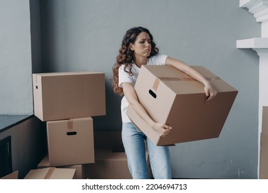 Tired young woman renter exhausted of carrying heavy cardboard boxes with things on moving day. Upset hispanic girl tenant frowning leaving rented apartment. Mortgage, real estate tenancy concept