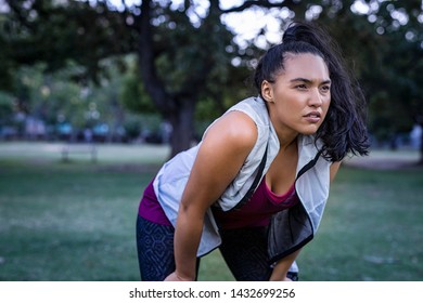 Tired young woman resting after jogging outdoor. Determined latin girl sweating and taking a rest after running hard. Exhausted curvy woman relaxing after running in park with breathing exercise.