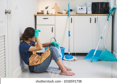 Tired young woman sitting on kitchen floor with cleaning products and equipment, Housework concept